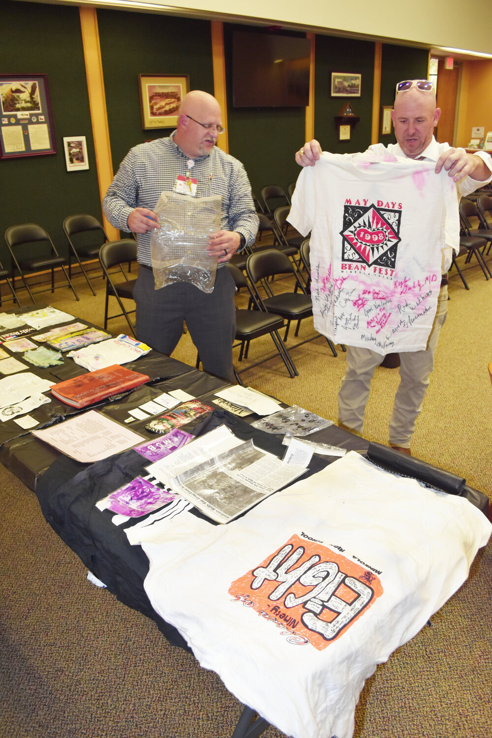 John Sheeran, left, and Owen Tiner examine a t-shirt from the 1998 Mineola Bean Fest, signed by city staff members, that was placed in a time capsule 25 years ago.